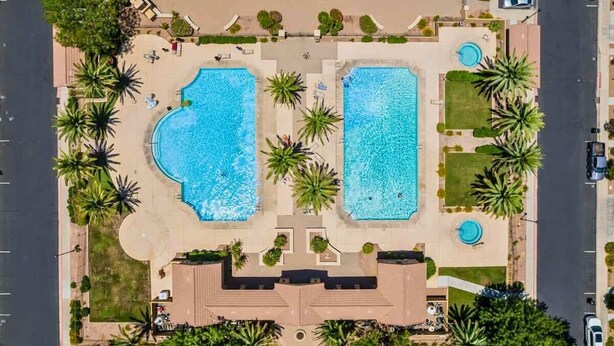 Ein Luftbild eines Resorts mit zwei großen, rechteckigen Pools, umgeben von Palmen und einem zentralen Weg.