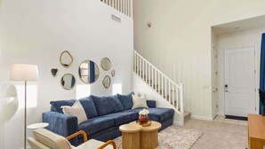 Ein Wohnzimmer mit einem blauen Sofa, zwei runden Couchtischen, einer Stehlampe und einer Treppe zu einer weiteren Ebene.