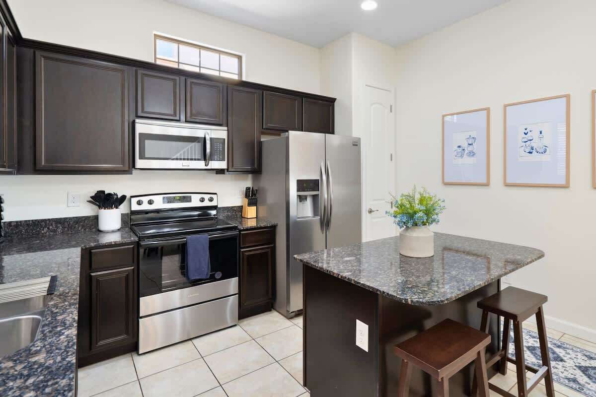 A modern kitchen with dark cabinetry, stainless steel appliances, a granite countertop, and a small island with stools.