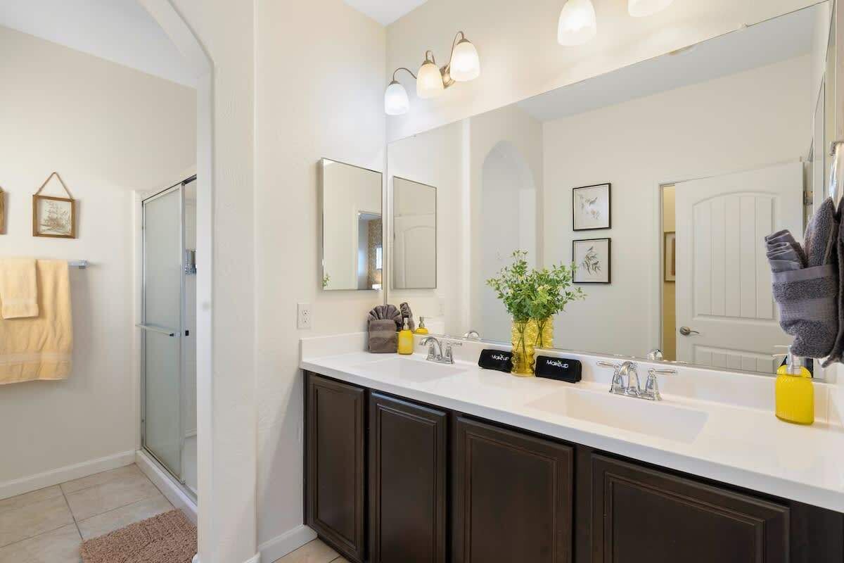 A modern bathroom with a double sink, dark cabinets, a large mirror, and a glass shower enclosure.