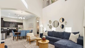 Ein modernes Wohnzimmer mit einem blauen Sofa, einem Essbereich mit blauen Stühlen und einer Küche im Hintergrund.