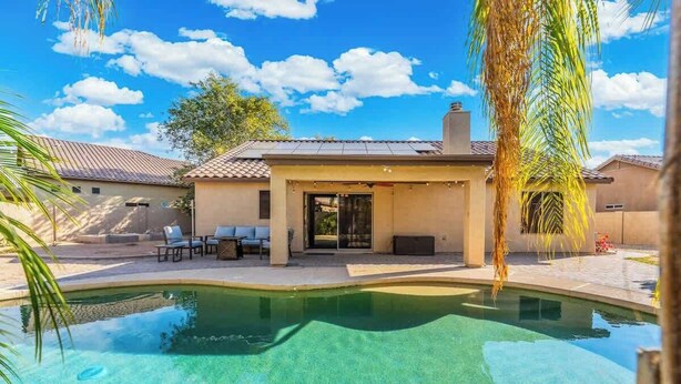 A swimming pool with a patio area, a covered seating area, and a building with a tiled roof.