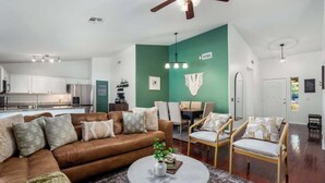 A modern living room with a brown leather sofa, two wooden chairs, a round coffee table, and a green accent wall.