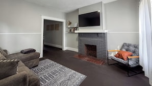A living room with a fireplace, a sofa, a chair, and a television mounted above the fireplace.