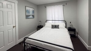 A bedroom with a bed, a nightstand, a bedside table, a door, and a painting on the wall.