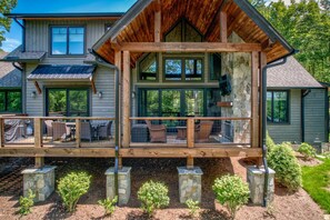 Ein zweistöckiges Haus mit einer Holzterrasse, Steinpfeilern und großen Fenstern.
