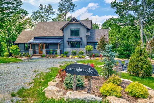 A two-story lodge with a prominent front porch, stone foundation, and a well-maintained garden.