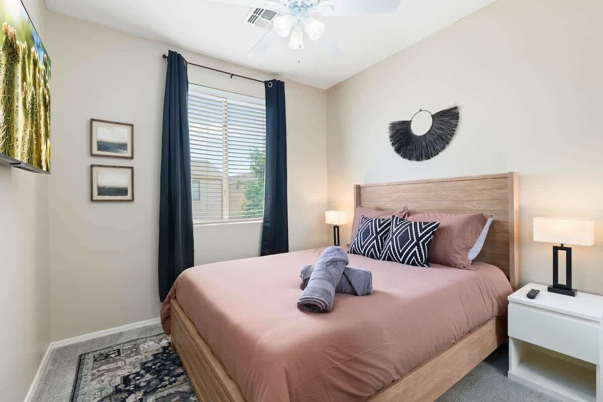 Una camera da letto ordinata con un letto, lampade da comodino, una ventola a soffitto e una finestra con tende.