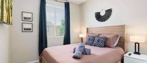 Una camera da letto ordinata con un letto, lampade da comodino, una ventola a soffitto e una finestra con tende.