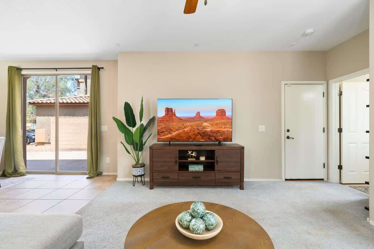 A living room with a flat-screen TV on a wooden cabinet, a coffee table with decorative balls, and a large plant.