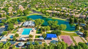Vue aérienne d’un quartier résidentiel avec une grande piscine, des courts de tennis et un parc doté d’un lac.