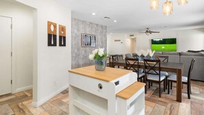 A modern living room with a dining area, a gray sofa, a TV, and a ceiling fan. - *NEW* Western Desert Pool Oasis! Fire Pit & Grill! (Glendale)