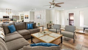 A modern living room with a sectional sofa, a coffee table, and a ceiling fan. - *NEW* Western Desert Pool Oasis! Fire Pit & Grill! (Glendale)
