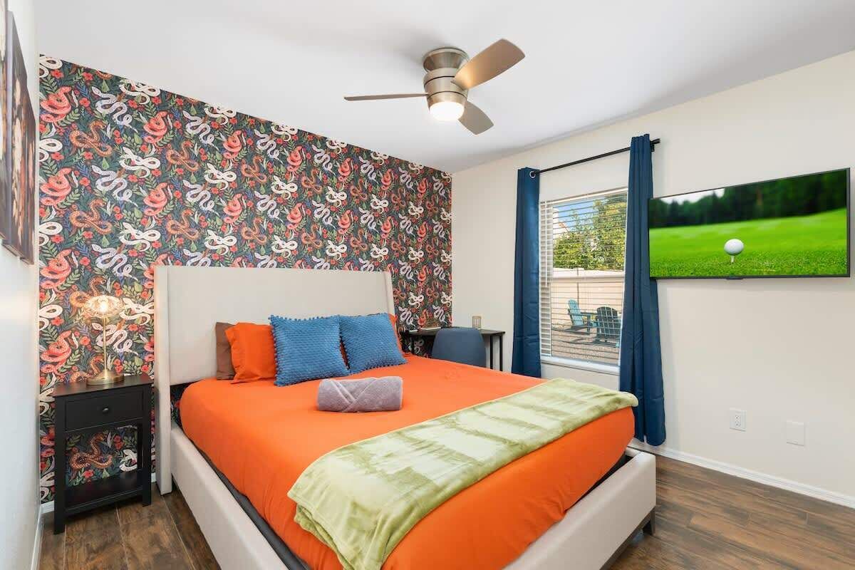 A bedroom with a bed, a ceiling fan, a TV on the wall, and a window with curtains.