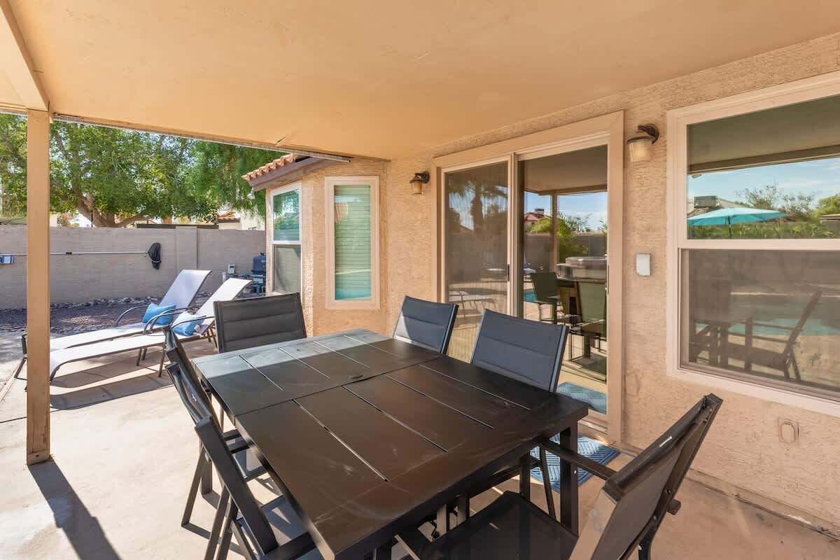 An outdoor patio with a dark metal table and chairs, a covered area with a beige canopy, and a sliding glass door leading to a pool area.