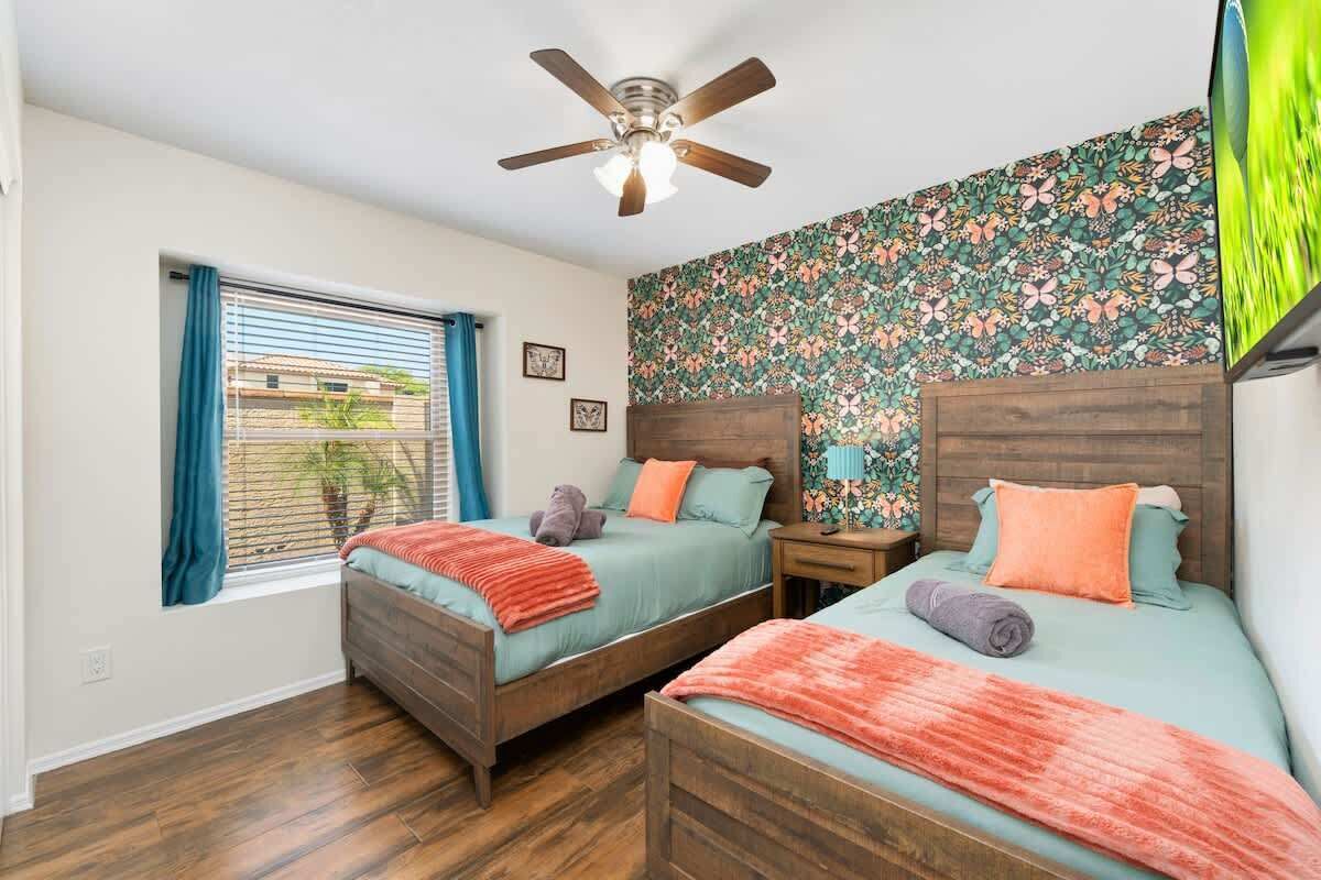 A bedroom with two beds, a ceiling fan, a window with curtains, and a floral wallpaper.