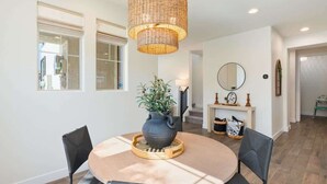 Un coin repas avec une table ronde, des chaises, un luminaire suspendu, une plante en pot et une cheminée surmontée d’un miroir.