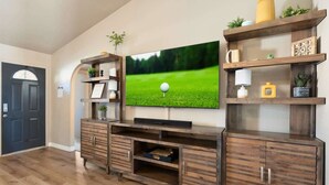 Een woonkamer met een flatscreen televisie aan de muur, een houten entertainmentkast met lades en planken met decoratieve objecten.
