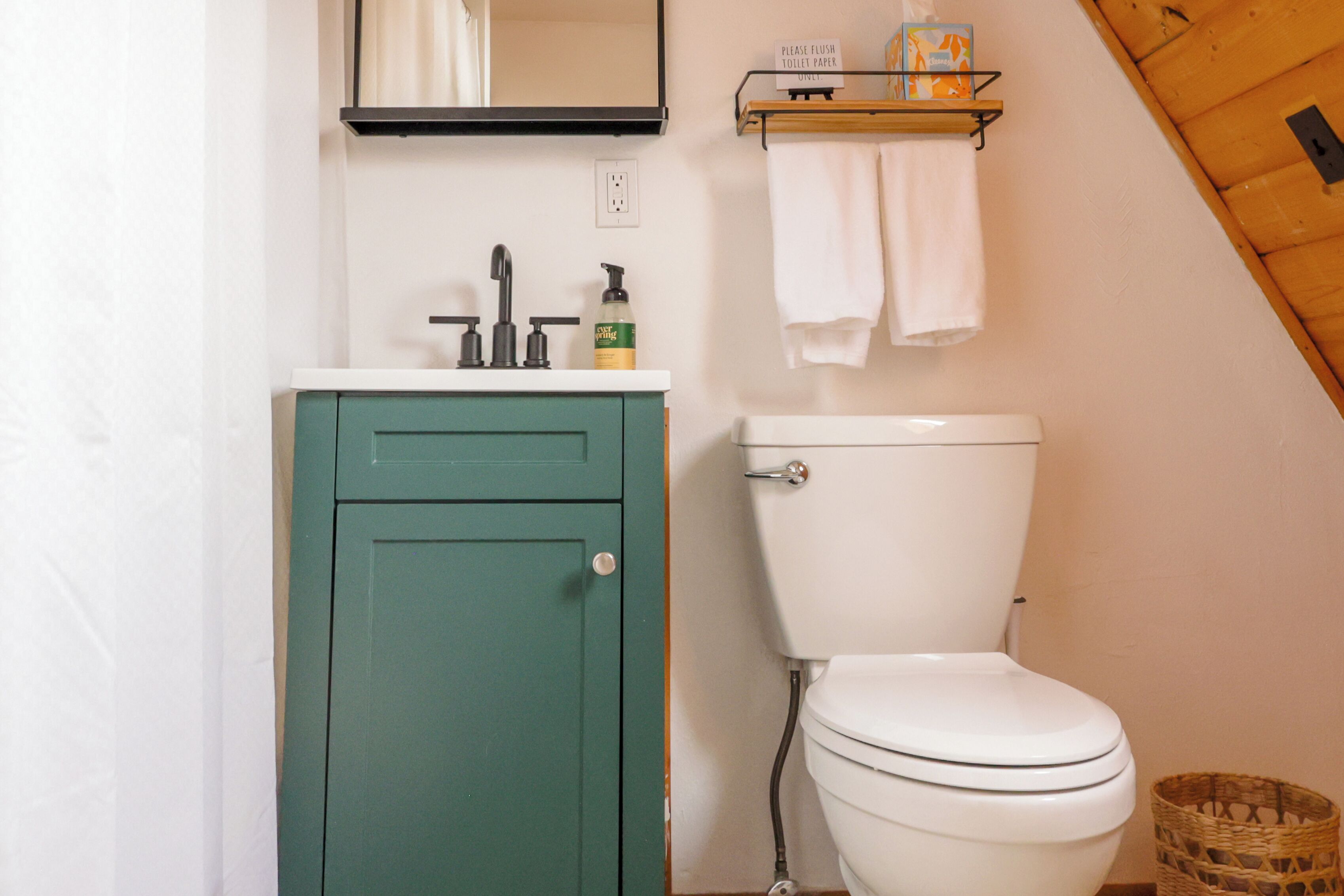Een badkamer met een groen kastje, een wit toilet, een spiegel en een plank met toiletartikelen.
