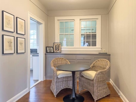 A dining area with wicker chairs and a round table, a window with frosted glass, and framed artwork on the wall.. Cozy Bungalow on Washington – Private Office