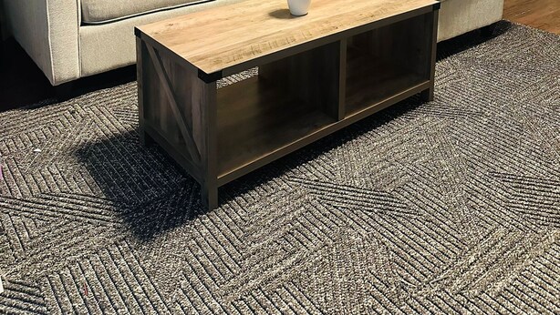Ett vardagsrum med en beige soffa, färgglada kuddar, ett soffbord i trä och en mönstrad matta.