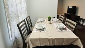 En matplats med ett bord dukat för fyra personer, stolar, en liten krukväxt och en tv-apparat i bakgrunden.