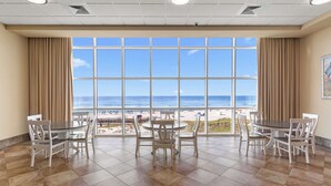 Habitación con un amplio ventanal con vistas a la playa, amueblada con una mesa redonda y sillas, y suelo de baldosas.