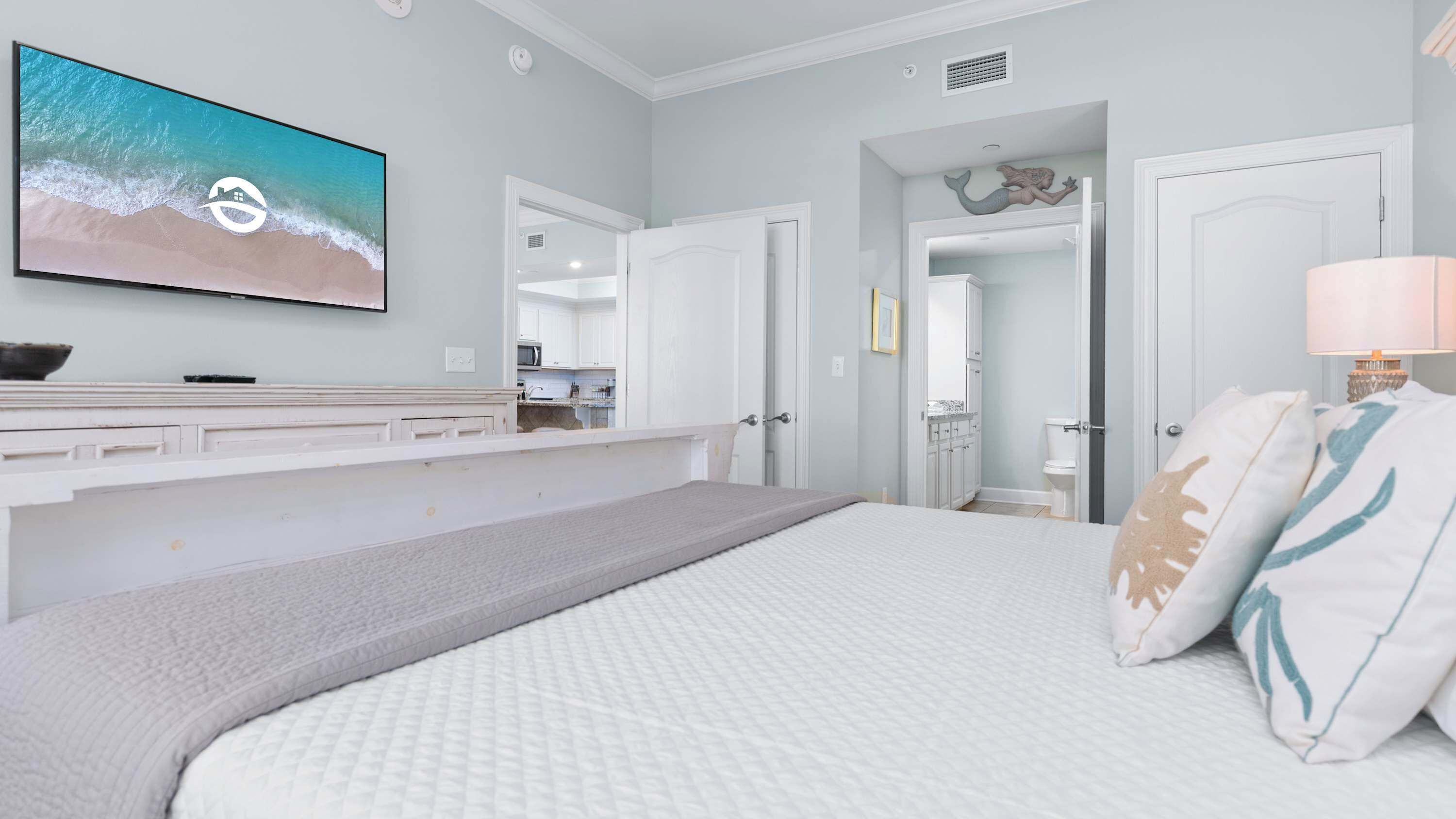 Een slaapkamer met een groot bed, een aan de muur bevestigde televisie en uitzicht op de badkamer door een geopende deur.