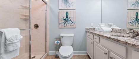 A bathroom with a glass shower enclosure, a toilet, and a vanity with a sink. There are three wall-mounted artworks depicting octopuses.