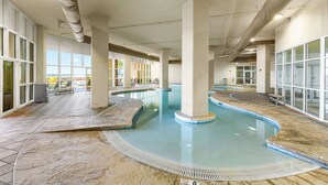 Una piscina interior con vistas despejadas a través de amplios ventanales, suelo de baldosas y techo con conductos a la vista.