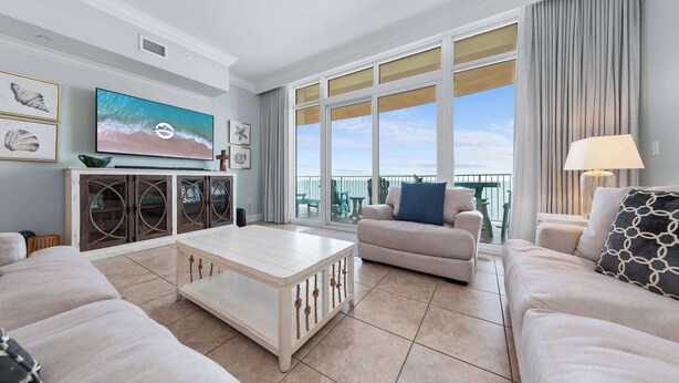 Un salón amplio con televisor grande, asientos cómodos y un balcón con vistas al mar.