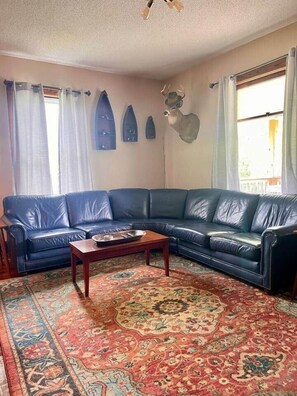 Una sala de estar con un sofá de cuero azul, una mesa de centro de madera, un tapete estampado y decoración mural.