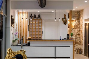 A reception area with a wooden counter, pendant lights, a stone wall, and a decorative shelf with items. - Art Hotel (Sarandë)