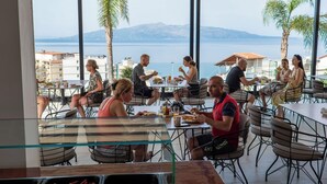 Zona pranzo all'aperto con tavoli e sedie, con vista su un corso d'acqua e montagne.