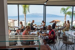 An outdoor dining area with tables and chairs, overlooking a body of water and mountains. - Art Hotel (Sarandë)