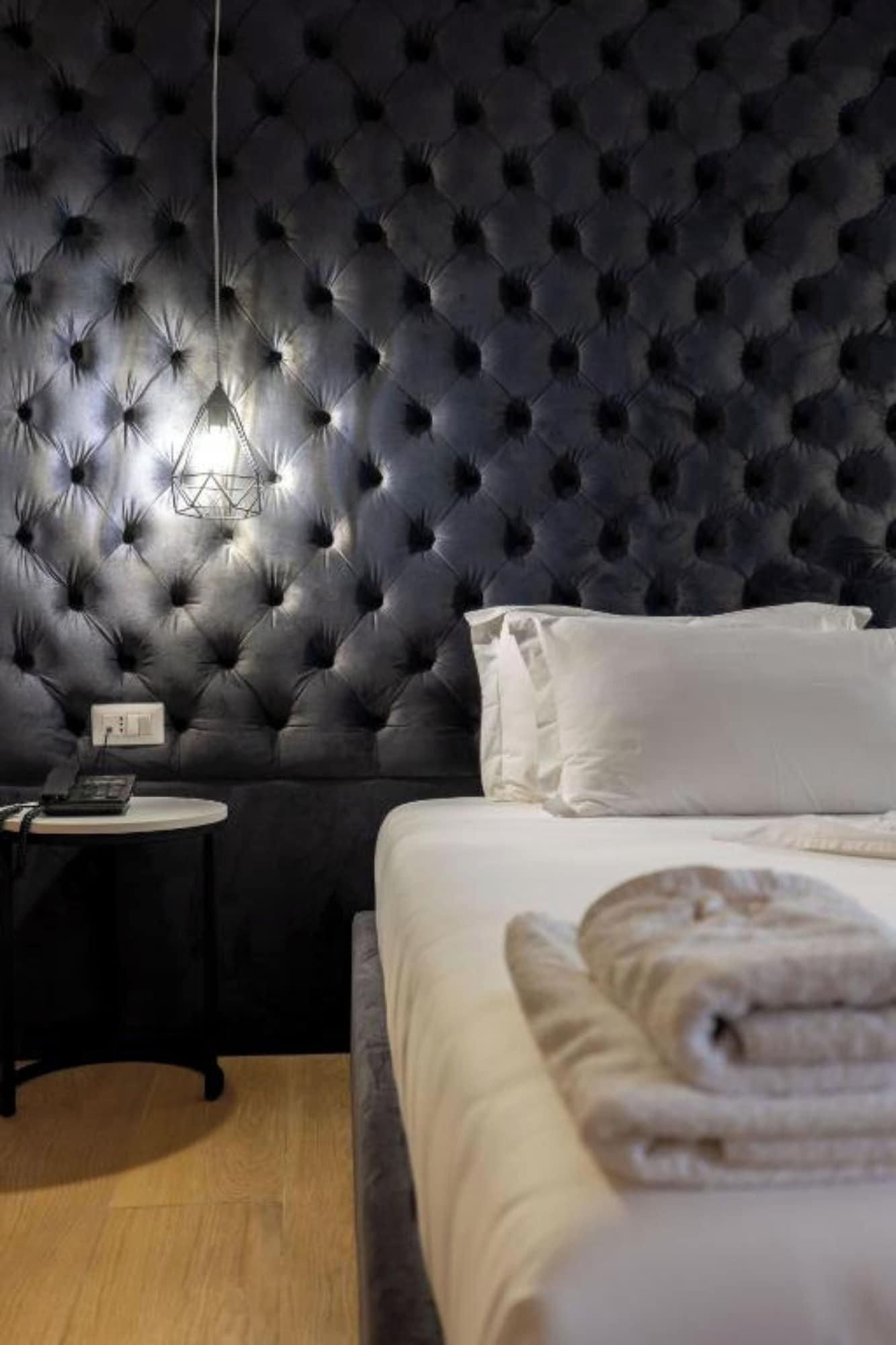 A bedroom with a tufted headboard, a bedside table with a lamp, a bed with white bedding, and a wooden floor.