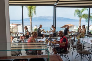 Un área de comedor al aire libre con mesas y sillas, con vistas a un cuerpo de agua y montañas.