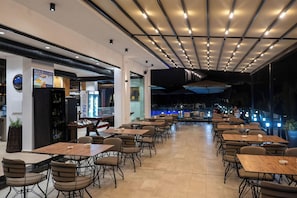 A spacious indoor dining area with multiple tables and chairs, a bar area with a refrigerator, and a view of a pool outside. - Art Hotel (Sarandë)