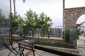 Varanda com mesa e cadeiras, parede de pedra e vista para o mar.