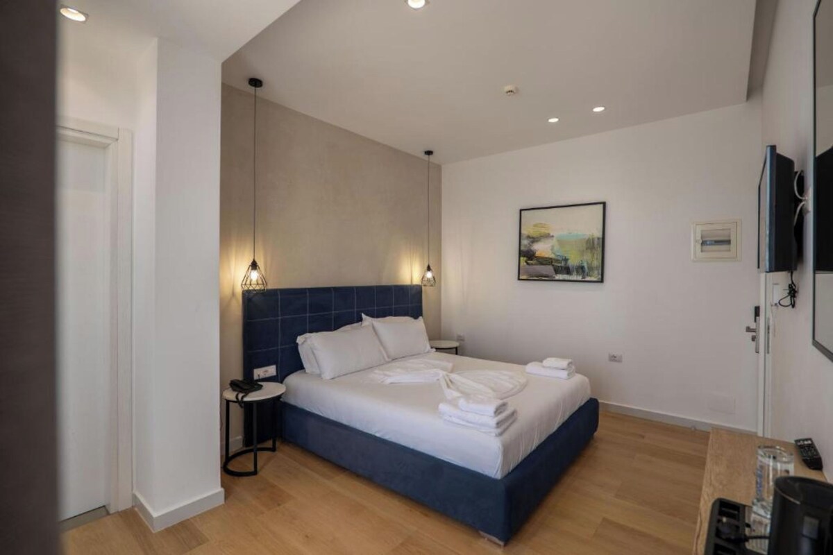 Una habitación de hotel moderna con una cama grande, mesitas de noche, un televisor de pantalla plana y un cuadro en la pared.