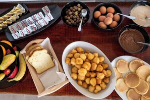 Ein Frühstücksbuffet mit verschiedenen Speisen, darunter Brot, Obst, Eier und Pfannkuchen.