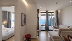 Una camera d'albergo moderna con un letto, uno sgabello rosso, un quadro e vista mare da un balcone.