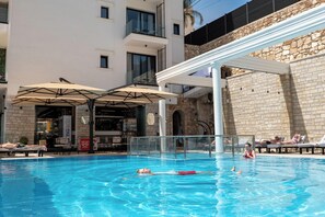 A swimming pool with lounge chairs and umbrellas, a bar, and a stone wall. - Art Hotel (Sarandë)