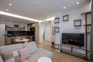 Uma sala de estar moderna com sofá, televisão e cozinha ao fundo.