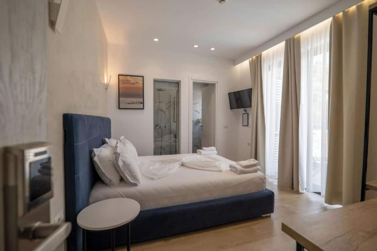A modern bedroom with a bed, a small round table, a TV, and a bathroom visible through a glass door.