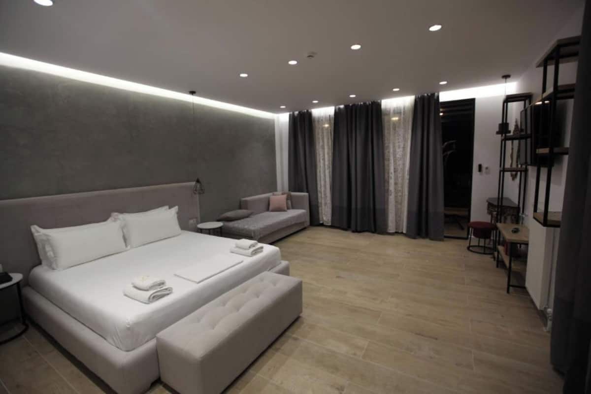 A modern bedroom with a large bed, a sofa, a small table, and a wardrobe.