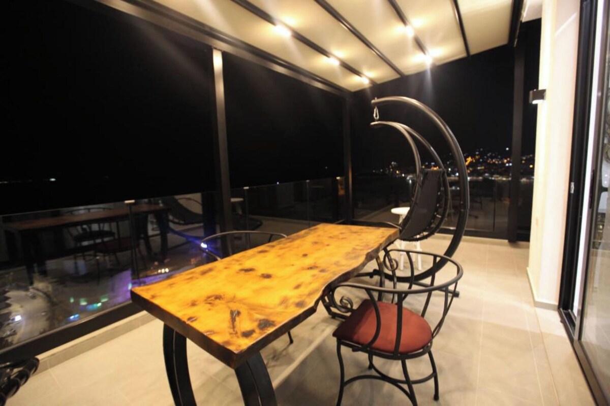 Un comedor moderno con mesa de madera y sillas de metal, con vista a un paisaje urbano nocturno.