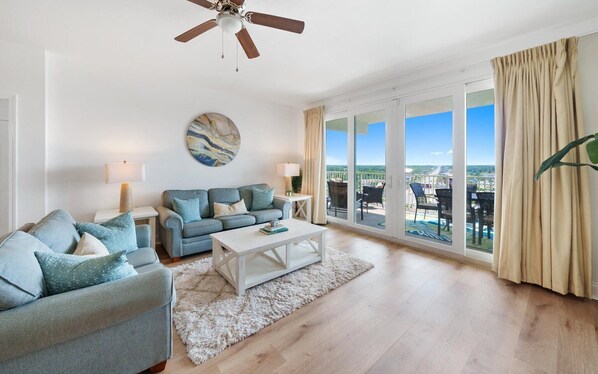 A spacious living room with a large window, a ceiling fan, and a view of the city.