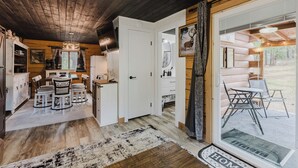 L’intérieur de ce chalet accueillant est doté d’un plafond en bois, d’un coin repas avec une table et des chaises, d’une cuisine équipée d’un réfrigérateur et de placards, ainsi que d’une grande porte-fenêtre coulissante donnant sur une terrasse extérieure.