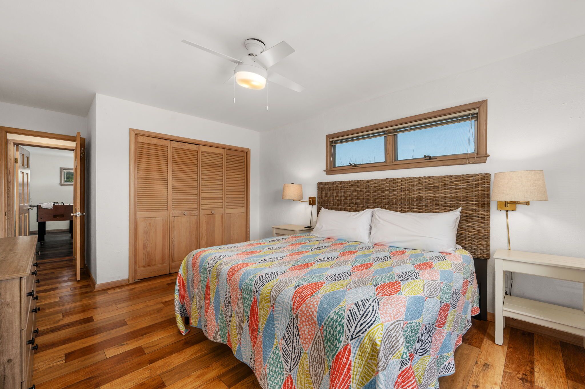 Une chambre à coucher comprenant un lit, une armoire en bois, un ventilateur de plafond, une fenêtre et des lampes de chevet.